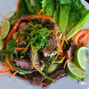 Grilled steak is served on a bed of spiral cucumber, romaine lettuce, carrots, cilantro with fresh mint and tossed in a flavorful lime juice dressing in this authentic Thai beef salad.