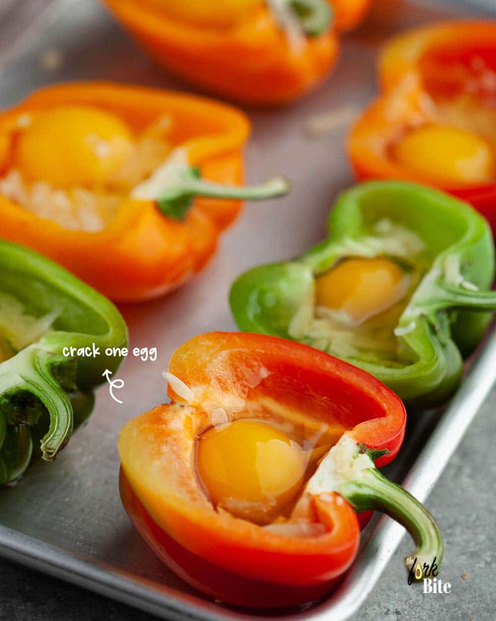 Once the  bell peppers are ready, take them out from the oven and crack an egg into each one.
