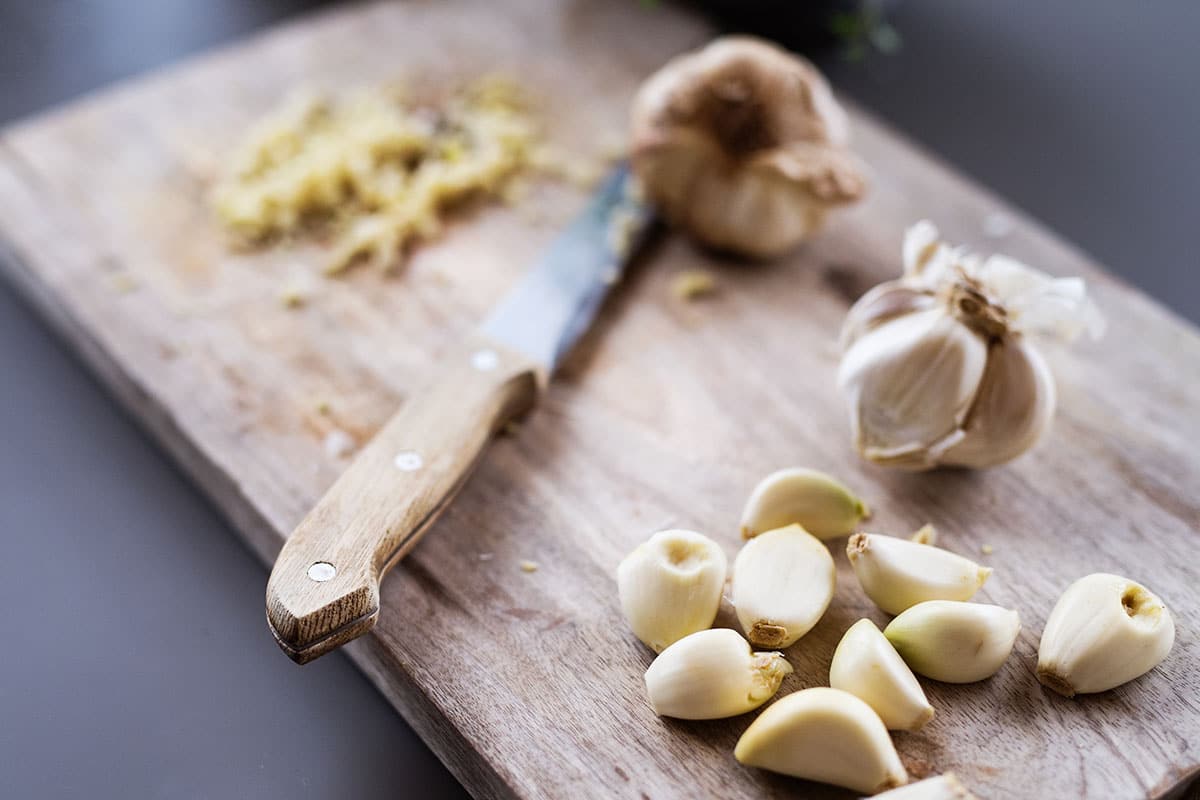 Place your clove of garlic onto a chopping board. Position the flat blade of your knife across the clove of garlic and press down until it bursts.