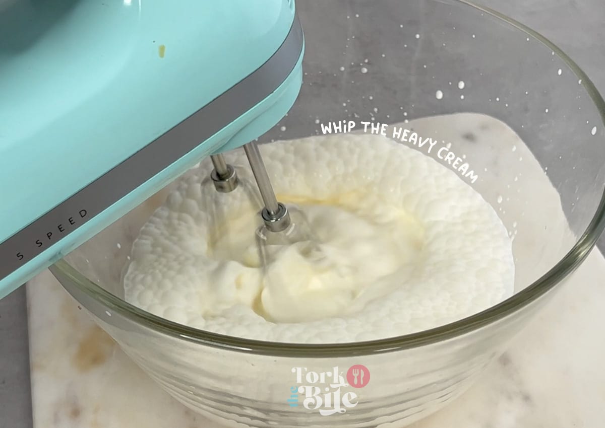 Whip the heavy whipping cream with an electric mixer until it forms soft peaks, creating a light and fluffy texture perfect for mixing with the pudding.