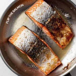 Flipping a salmon fillet in a pan, showing the seared, golden-brown skin