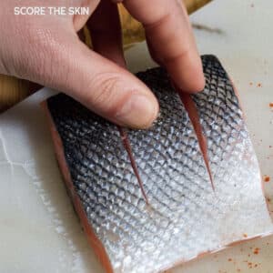Close-up of a hand using a sharp knife to score a salmon fillet with a crosshatch pattern