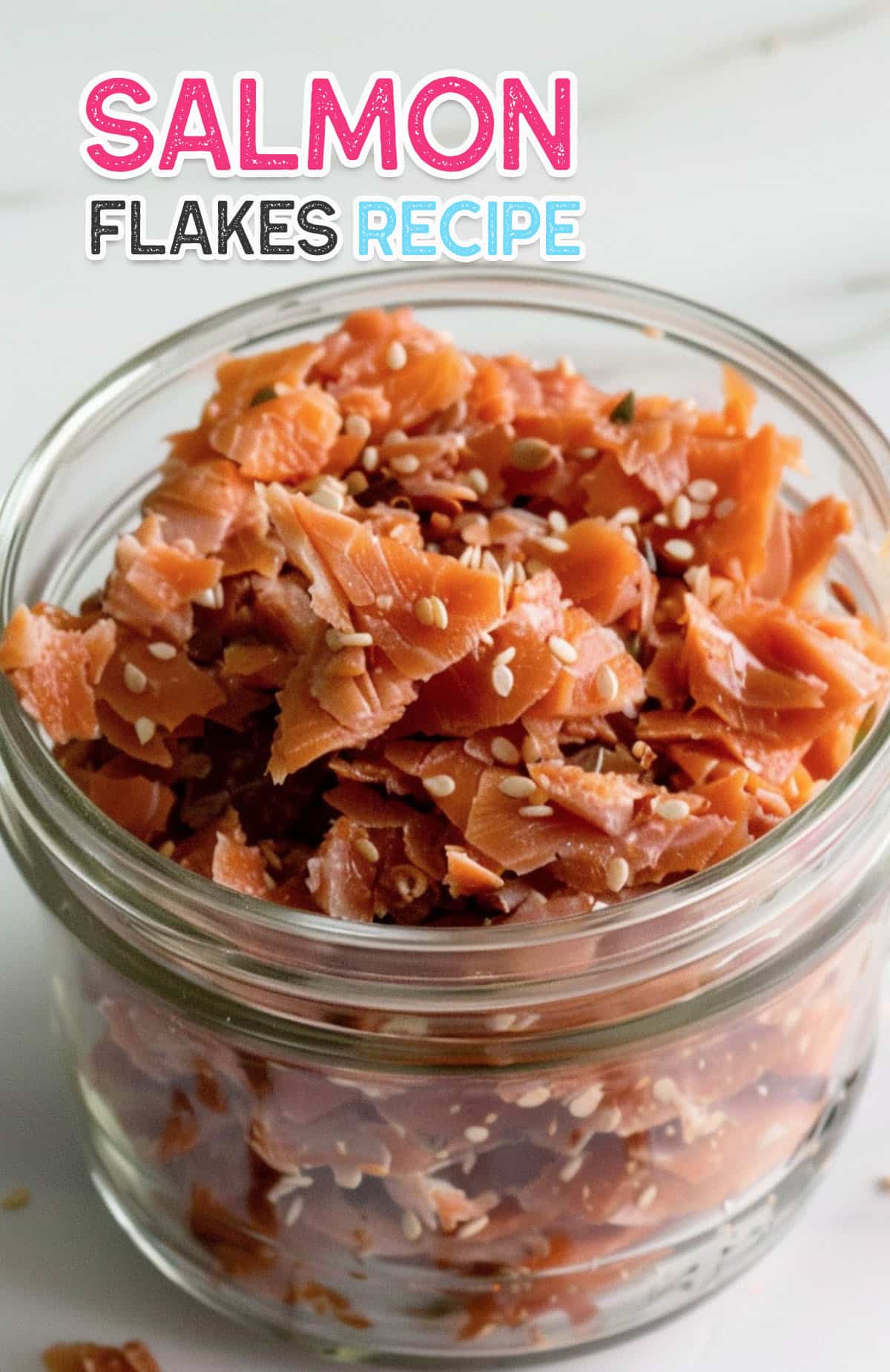 Close-up of pink, flaky salmon flakes in a glass jar, ready for recipes.