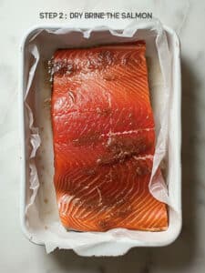 Close-up of a salmon fillet being coated in a dry brine of salt and brown sugar.