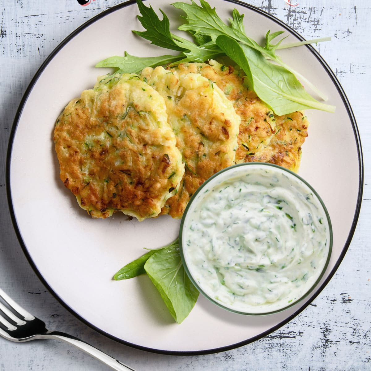 Creamy, white tzatziki sauce with a vibrant green swirl of fresh herbs.