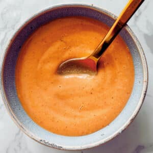 Dipping a spoon into Chipotle Tahini sauce for a taste test and flavor adjustments