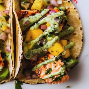 A plate of vibrant air fryer salmon tacos topped with mango salsa and fresh herbs.