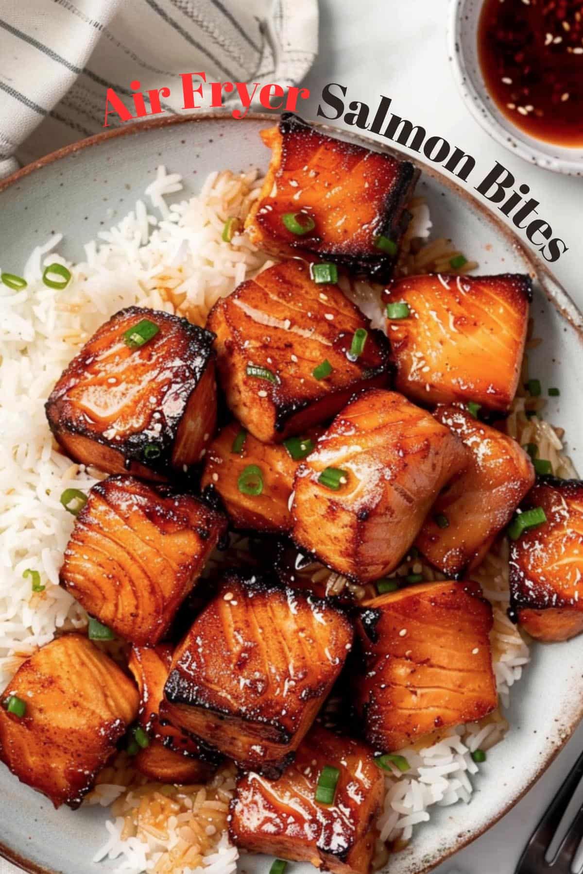 Close-up of golden-brown air fryer salmon bites on a plate, with a small dish of dipping sauce