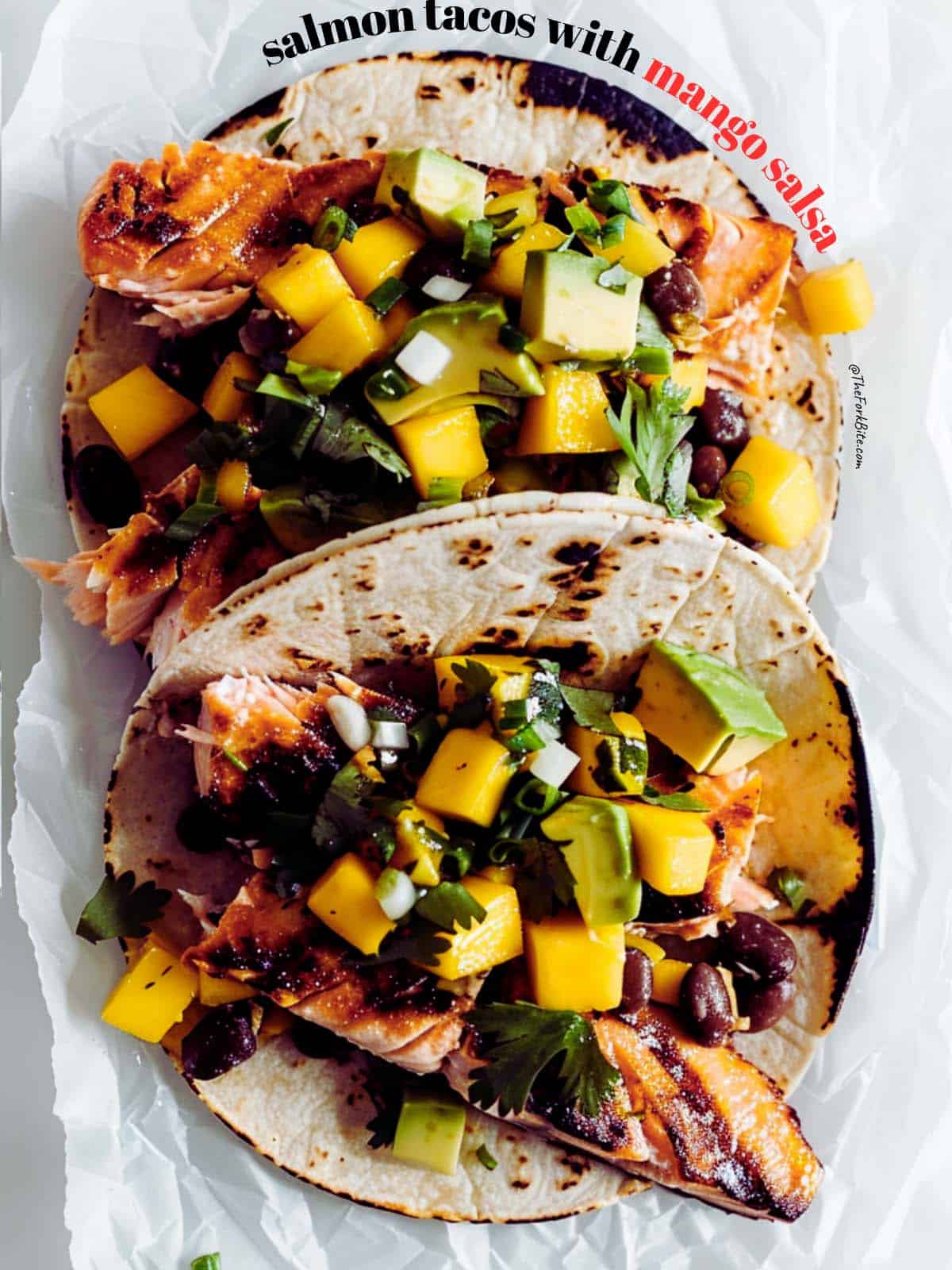 Assembled air fryer salmon tacos with corn tortillas, flaky salmon, and mango salsa.