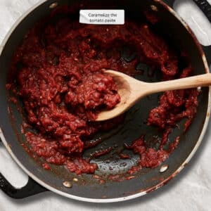 Tomato paste in a skillet, caramelizing from bright red to a deep, rich red color with constant stirring.