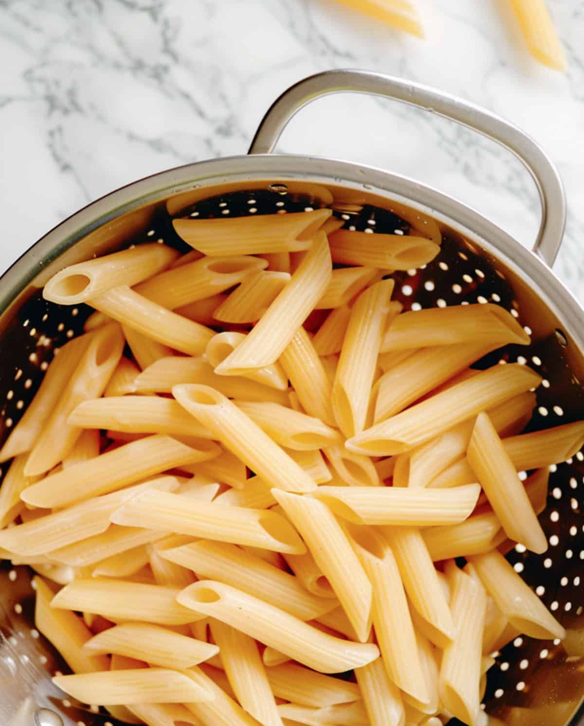 Close-up of cooked pasta in a colander showcasing al dente texture; noodles are firm and slightly separated, not mushy.