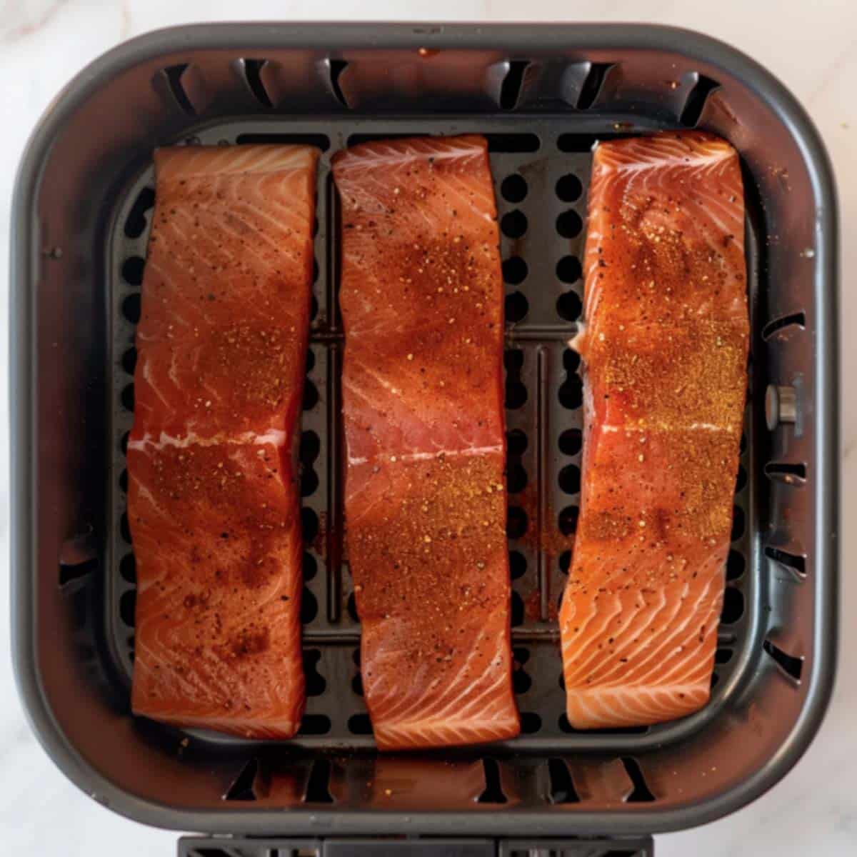 Salmon fillets in an air fryer basket, ready to cook into delicious air fryer salmon tacos.