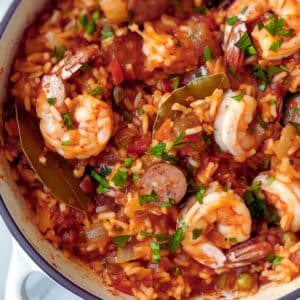 Close-up of Jambalaya in a cast-iron skillet, showing shrimp, sausage, peppers, celery, and rice in a rich, tomato-based sauce.
