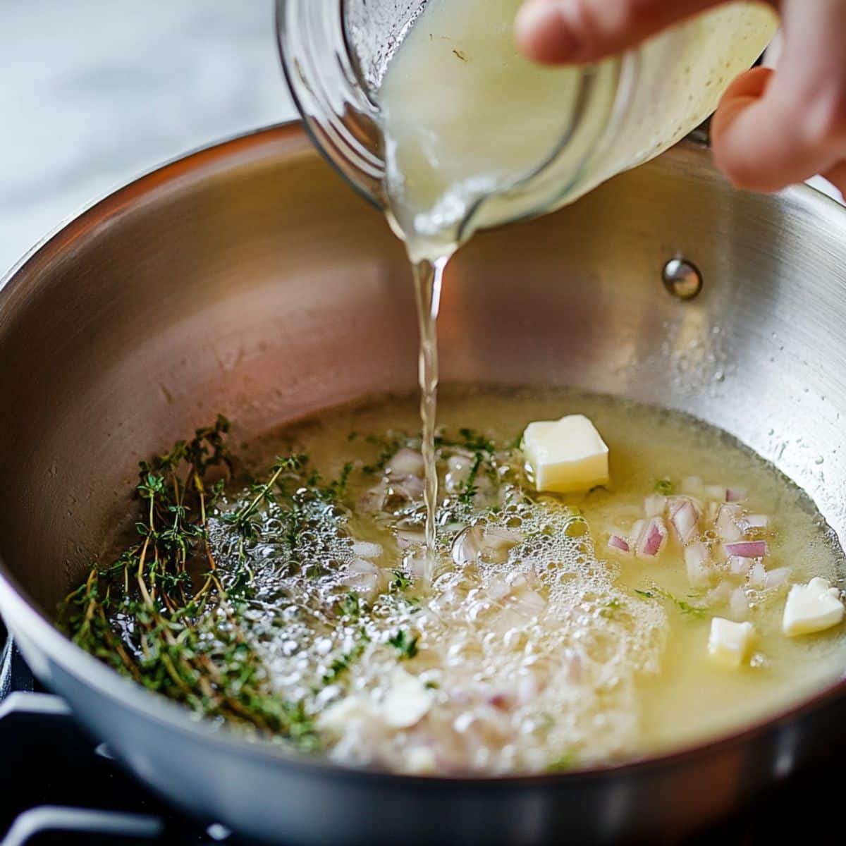 Pouring broth into a pan with butter, shallots, and fresh thyme.