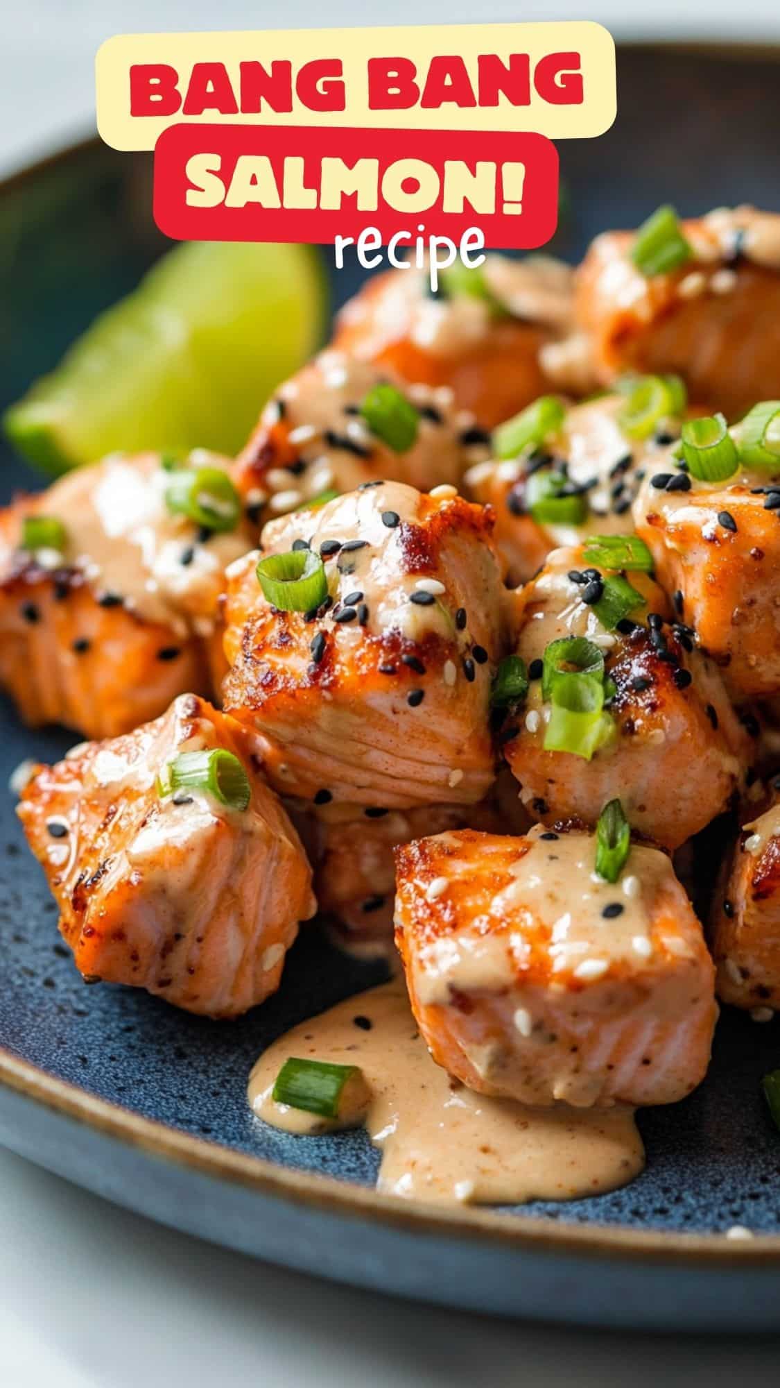Crispy Bang Bang Salmon bites coated in a creamy, spicy sauce, garnished with sesame seeds, green onions, and red pepper flakes, served with lime wedges on a blue plate.