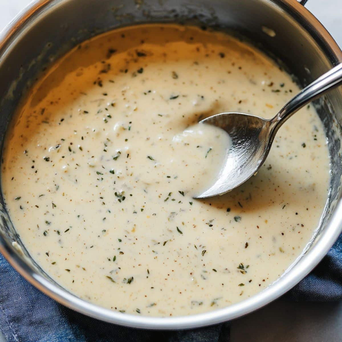 Creamy butter lemon herb sauce in a saucepan with a spoon.